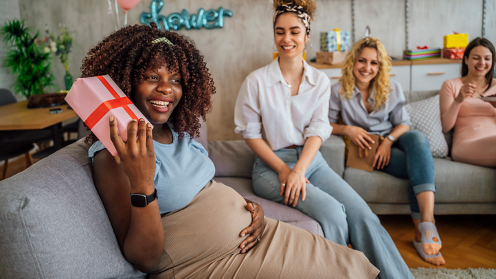 A pregnant woman at her baby shower smiling as she opens a gift