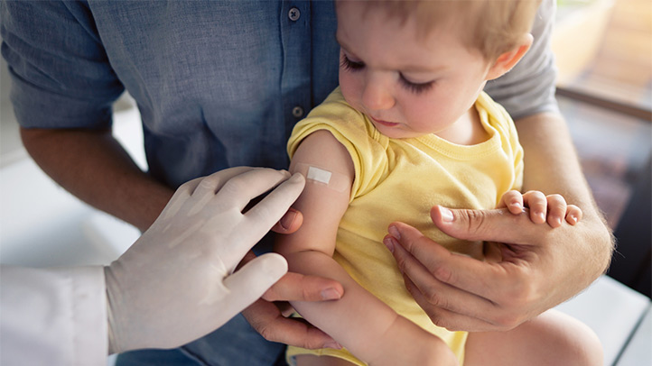 kids and covid-19 vaccines, baby at doctor's looking at vaccine bandage