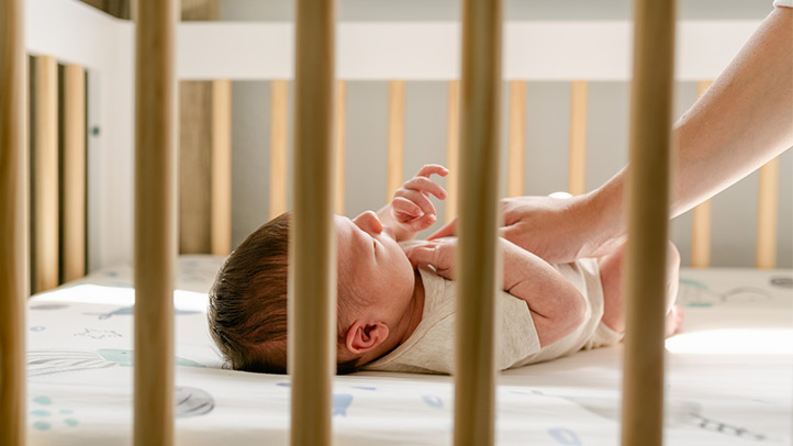 parent's hand resting on baby's chest in crib