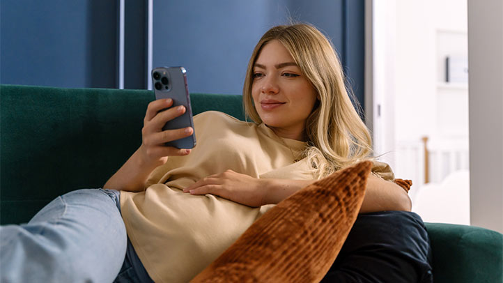 pregnant mom sitting on a green sofa looking at her phone